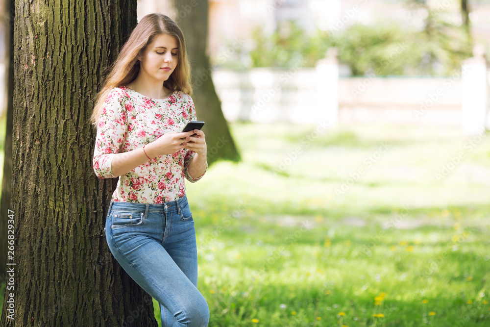 Beautiful blonde women leaning on the tree while using her phone Beautiful blonde women leaning on the tree while using her phone