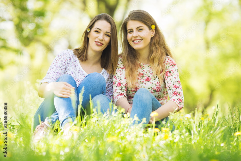 Two female friends sitting in grass and smiling Two female friends sitting in grass and smiling