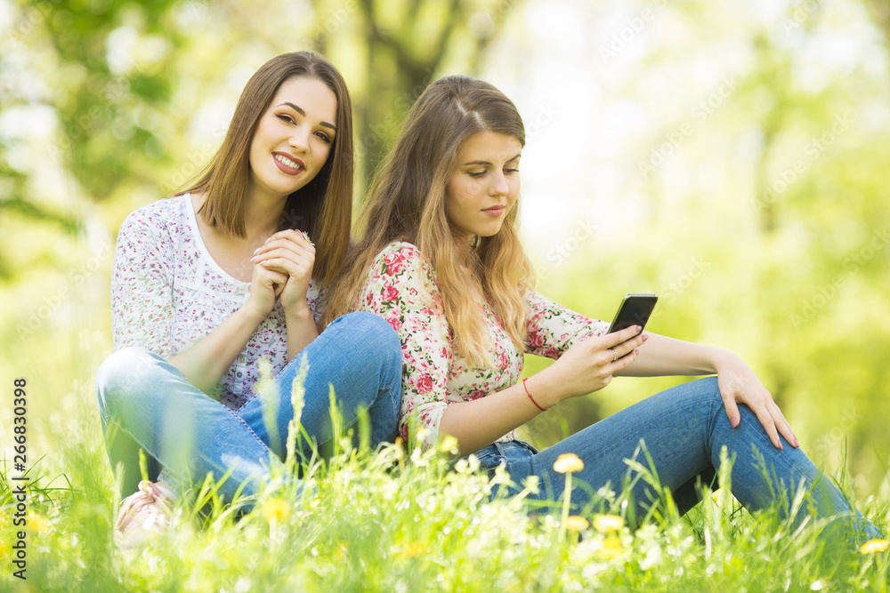 Two young women sitting in grass and enjoying their day Two young women sitting in grass and enjoying their day