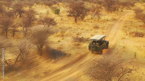 Aerial of a safari jeep traveling on the plains of Africa, at Erindi Game Preserve, Namibia with native San tribal spotter guide sitting on front spotting wildlife. photo
