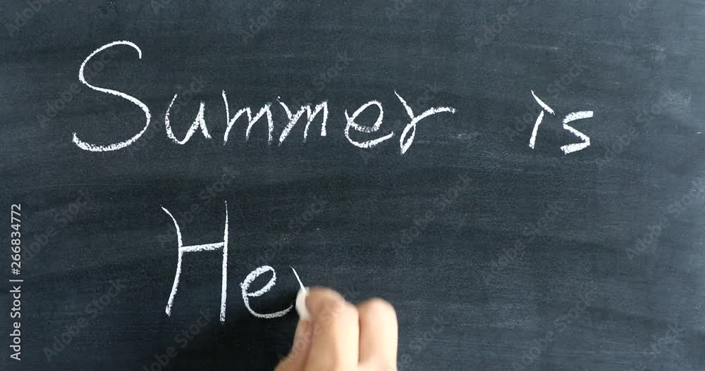 Writing SUMMER IS HERE on chalkboard with white chalk Writing SUMMER IS HERE on chalkboard with white chalk