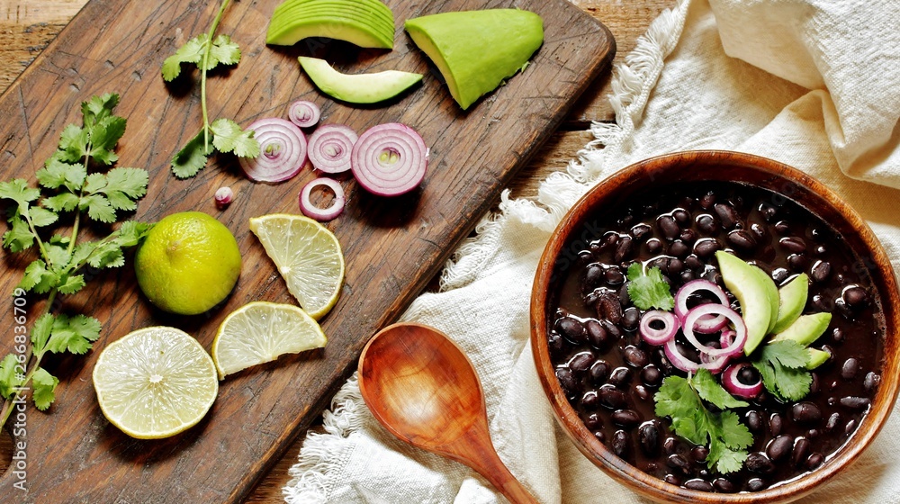 thick black bean soup or stew. Latin American or Mexican cuisine. stewed black beans served with avocado and red onion and cilantro. place for text. top view.