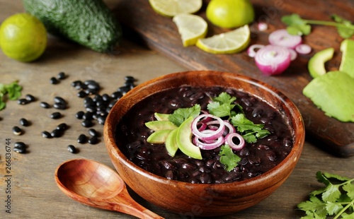 black bean soup or stew. Latin American or Mexican cuisine. stewed black beans served with avocado and red onion and cilantro.