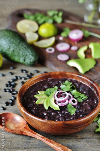 black bean soup or stew. Latin American or Mexican cuisine. stewed black beans served with avocado and red onion and cilantro.