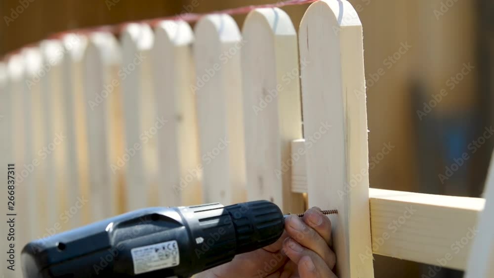 man building a wooden fence using an electric screwdriver