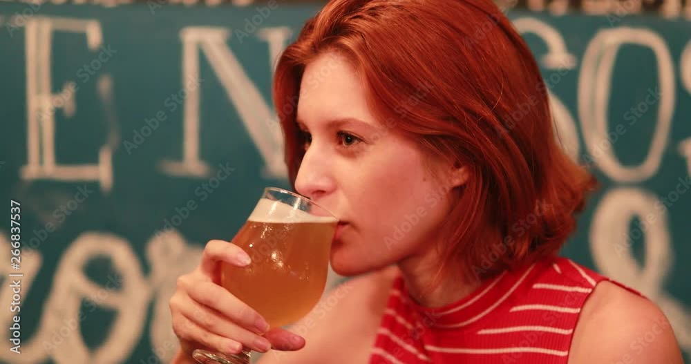 Casual redhead young woman drinking traditional draft beer at pub