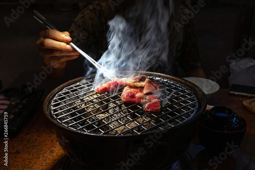 Female hand holding chopsticks picking up charcoal grilled beef