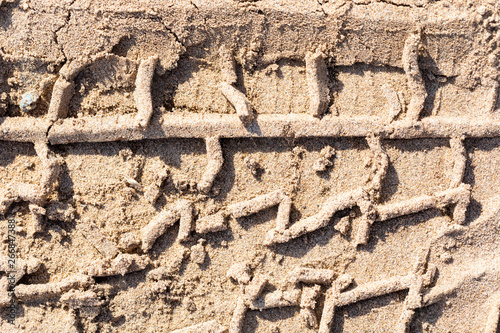 Print of a protector of tires of the car in crude sand on the river bank with various blades. Macro.