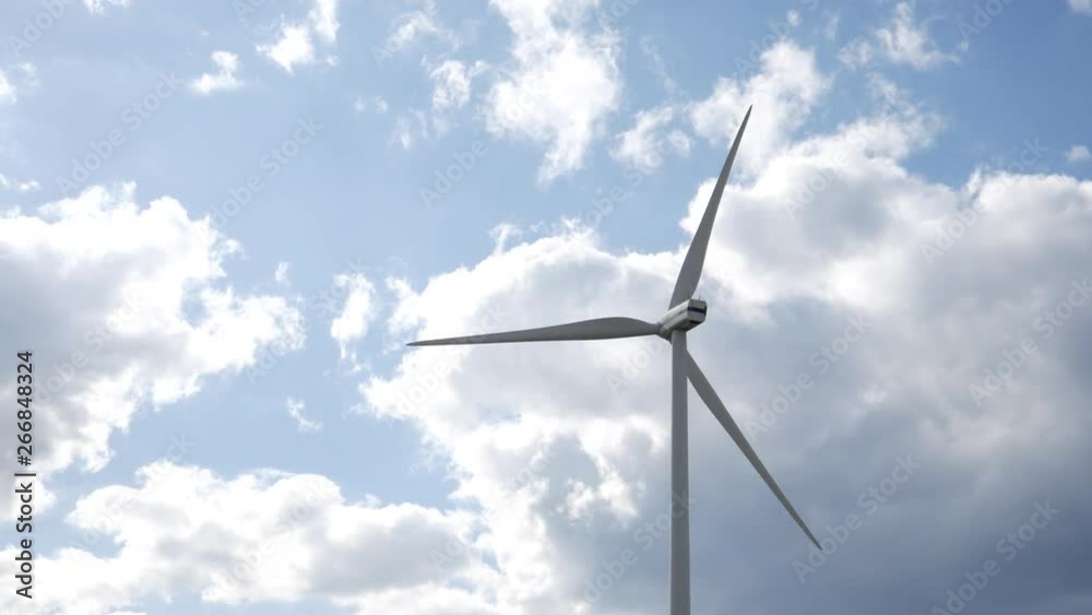 A rotating windmill on a field in the nature. Sunny day with huge clouds in the background and a blue sky.