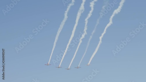 Five vintage war planes fly in formation leaving contrails behind in the blue sky