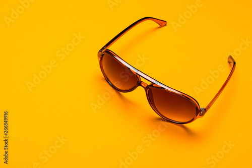 Eye care and diseases concept, eye protection. Brown plastic dark sunglasses over the orange background.