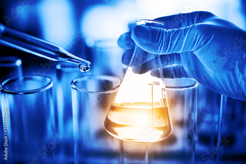 Flask in scientist hand with lab glassware background in laboratory. Science or chemical research and development concept.