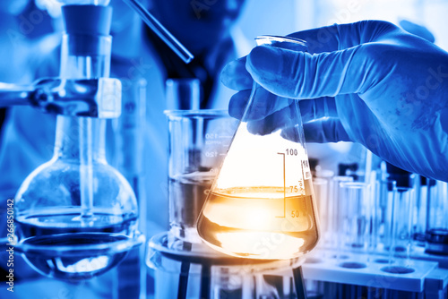 Flask in scientist hand with lab glassware background in laboratory. Science or chemical research and development concept.