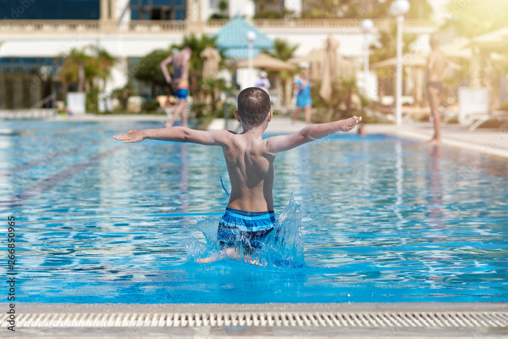 European boy in jumping into swimming pool at resort. Moment of entrance in water.