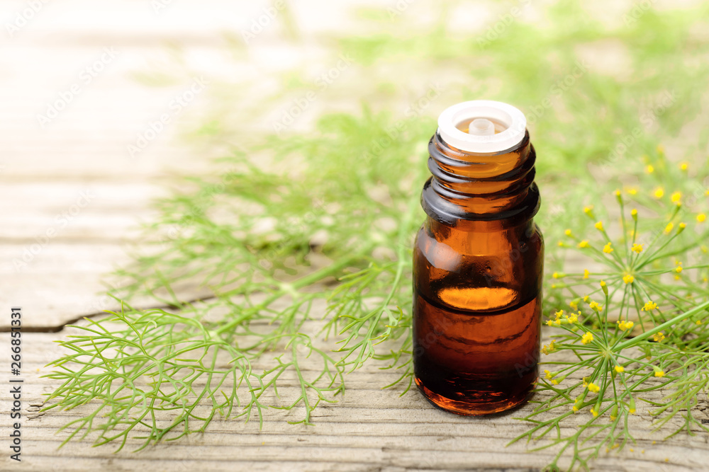 Fennel essential oil in the amber bottle with fennel flowers on the wooden board Fennel essential oil in the amber bottle with fennel flowers on the wooden board