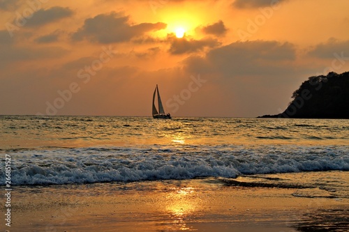 Agonda Beach by Sunset with sailboat on the Ocean and cliff, Goa, India photo