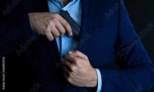 Man drawing his gun from coat pocket © SZ Photos