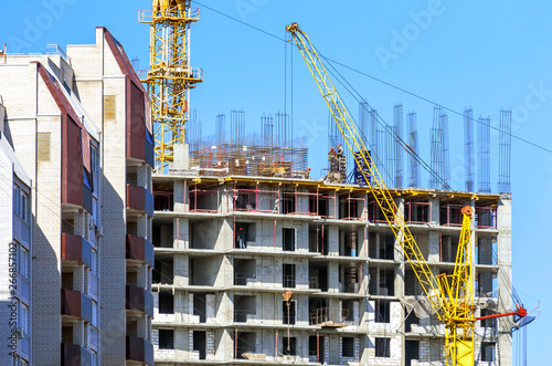 Finished Apartment Building and a New High-Rise Building Construction Site with Yellow Cranes against Blue Sky. Real Estate, Residential Buildings Urban Mixed-Use Development Concept.