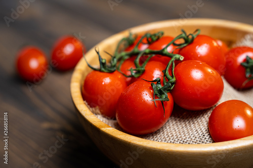 Fresh cherry tomatoes in a plate on a dark wood background.