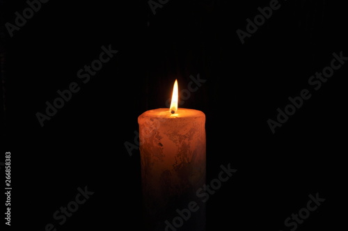 a large candle burns in the dark. On a black background