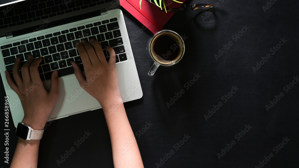 Top view of female hands with laptop typing on dark leather desk and copy space