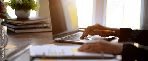 Young businesswoman is sitting at table, working on laptop with graphs, charts on paperwork