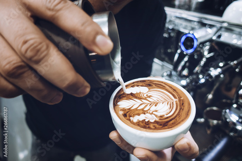 Barista s hand pouring milk to make latte art on cappuccino coffee