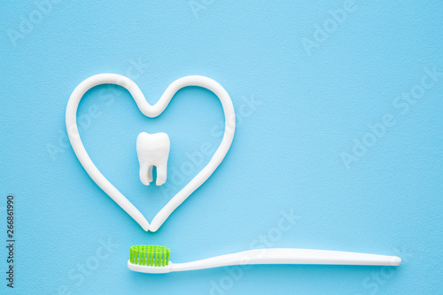 Toothbrush with green bristles on pastel blue background. Heart shape created from paste. White tooth in middle of heart. Love healthy teeth. Empty place for text, quote, sayings or logo. Closeup. photo