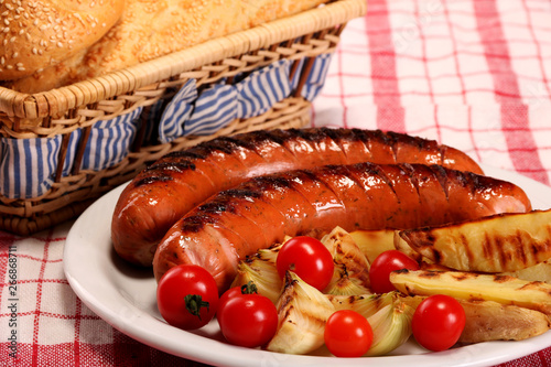 Grilled bbq sausages with vegetables, spices and bread in white plate on table