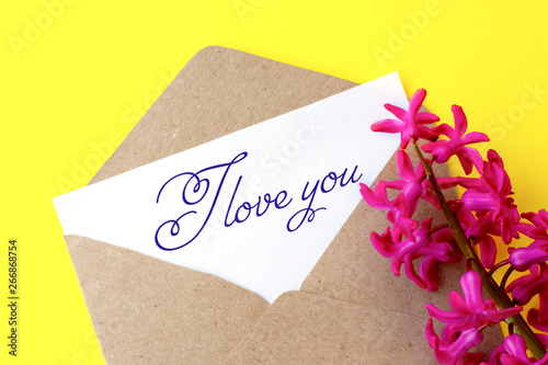 Love envelope and letter with written words I love you with pink hyacinth flowers on bright yellow bacground.
