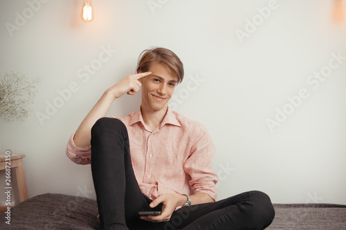 Portrait of pleasant looking young male model has clever expression, keeps finger on temple, has gentle smile. With smartphone. remembers himself not to forget tell important thing. Concept joy, smart photo