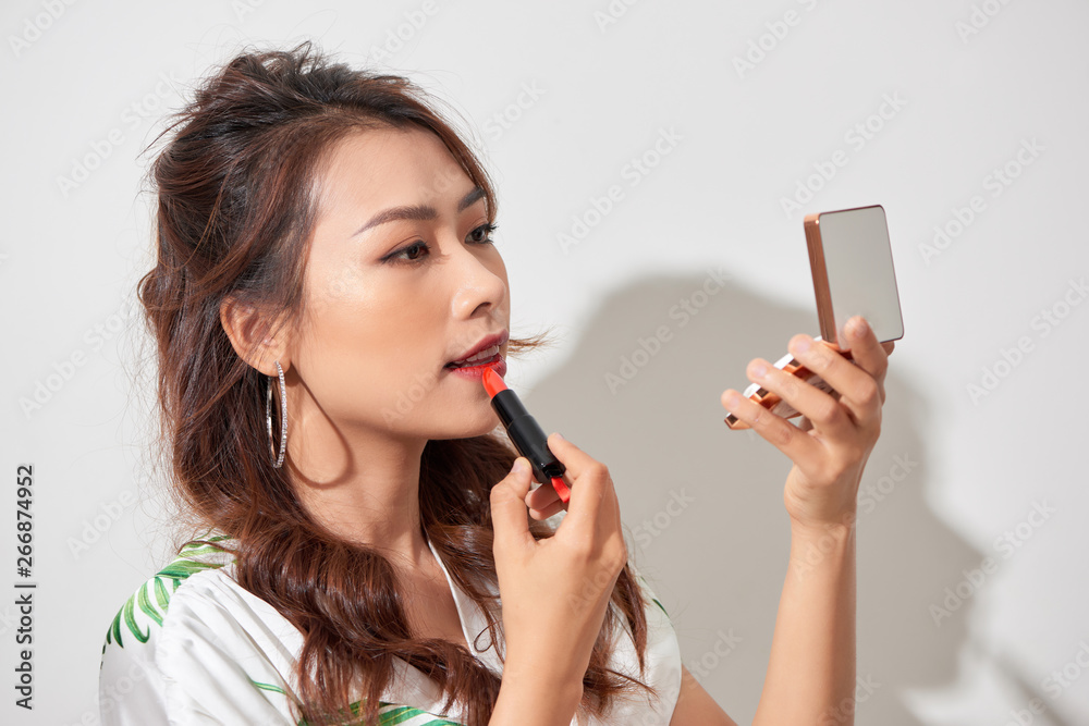 Attractive young woman refreshing her makeup lipstick by holding a handheld mirror powder box on a sunny day Attractive young woman refreshing her makeup lipstick by holding a handheld mirror powder box on a sunny day