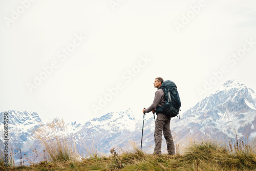 Man hiker in the mountains with a backpack, standing in profile. Active healthy lifestyle. Solo adventure journey. Wild trek. Space for text
