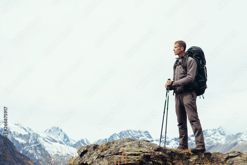 Male tourist in the mountains with a large backpack against the sky in cloudy weather. Space for text