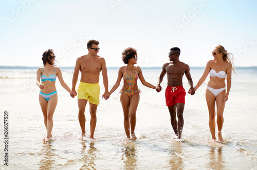 friendship, summer holidays and people concept - happy friends walking along beach