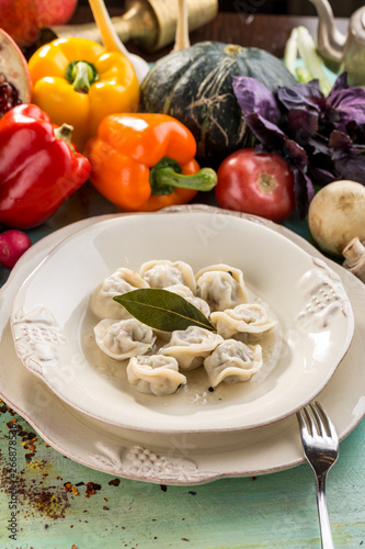 Russian meat dumplings pelmeni with bay leaf and fresh vegetables on blue wooden table