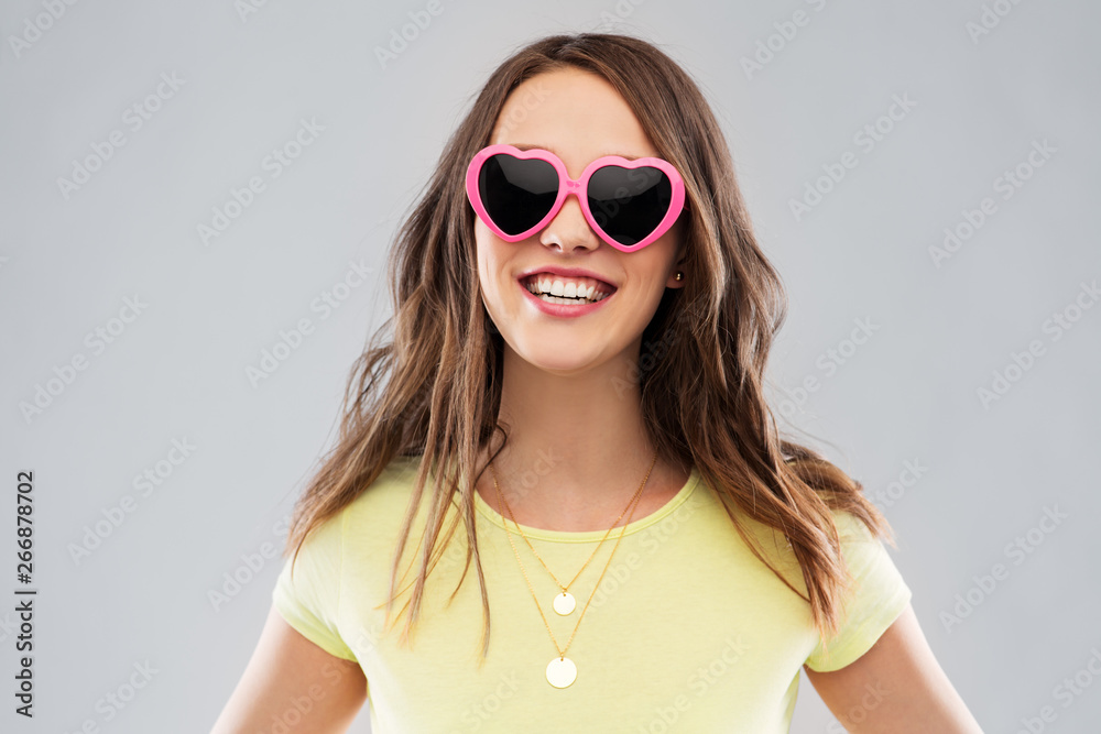 summer, valentine's day and people concept - smiling young woman or teenage girl in yellow t-shirt and heart-shaped sunglasses over grey background summer, valentine's day and people concept - smiling young woman or teenage girl in yellow t-shirt and heart-shaped sunglasses over grey background