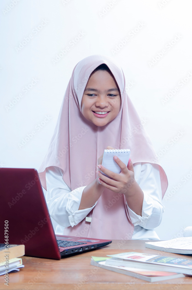Portrait of confident young woman smilling when working in her office with her red laptop, and writting on her notebook Portrait of confident young woman smilling when working in her office with her red laptop, and writting on her notebook