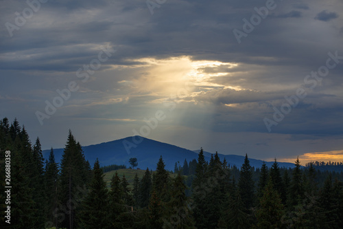 Sun shines through the gap in overcast dramatic sky over mountains