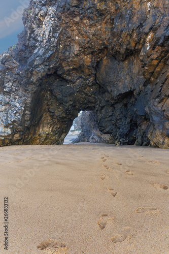 footprints barefoot from under the opening in the rock on a sandy beach at Cape Roca in Portugal