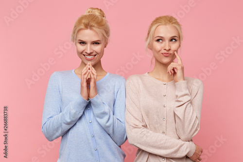 Beautiful young blonde twins conceived something interesting and do not want to disclose their secret to anyone. Look mysterious and thoughtful isolated over pink background.