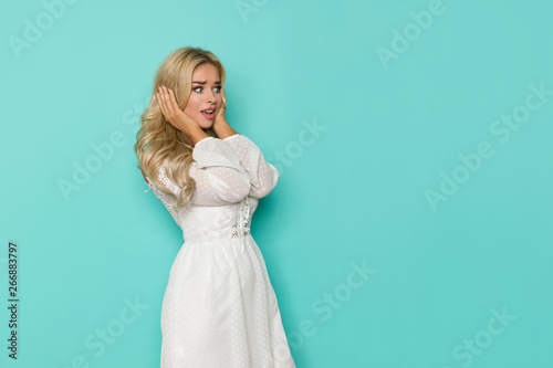 Shocked Beautiful Blond Woman In White Dress Is Holding Head In Hands And Looking Away