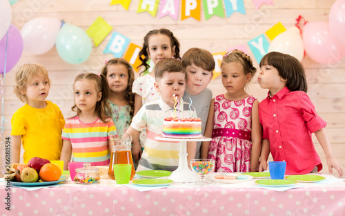 Group of children blowing candles on tasty cake at birthday party
