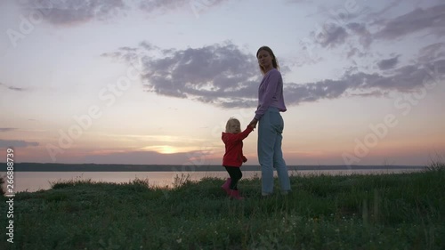 Cinematic portrait of young mother and her little daughter at sunset on field near seashore, slow motion photo