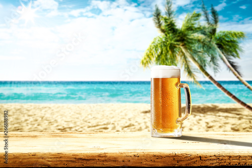 Summer background of wooden desk and cold beer. Free space for your decoration. Beach landscape with palms and ocean. Summer sunny day with sun light. Beach party and summer time.  © magdal3na