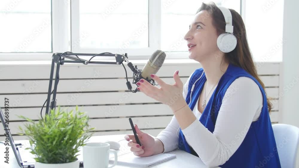 Concept of streaming and broadcasting. Young woman wearing headphones and talking at online radio station Concept of streaming and broadcasting. Young woman wearing headphones and talking at online radio station