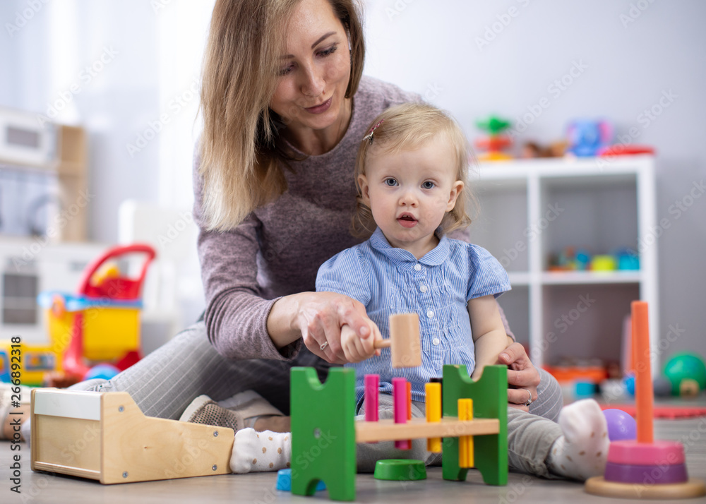 Adorable baby and babysitter playing with educational toys in nursery. Happy healthy child having fun with colorful different toys at home. Adorable baby and babysitter playing with educational toys in nursery. Happy healthy child having fun with colorful different toys at home.