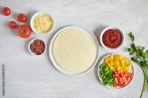 Fresh dough pizza base and ingredients on a white table. Top view.