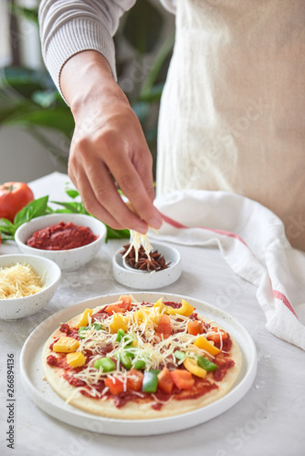 Fototapeta Naklejka Na Ścianę i Meble -  Baker's hand placing ingredients on pizza