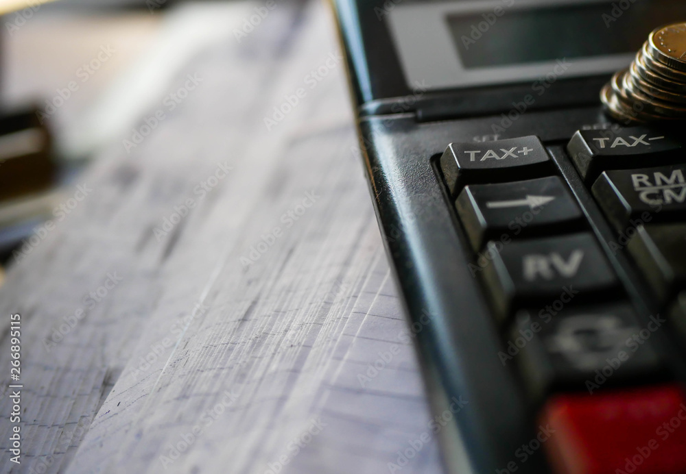 Used calculator with stack of coins, focus on the tax word, conceptual image of increasing taxes.